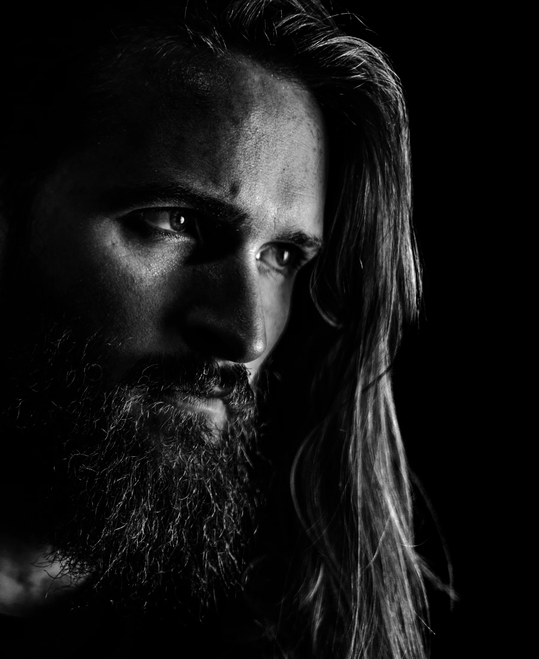 Black and white portrait, with a narrow light revealing the face against deep shadow